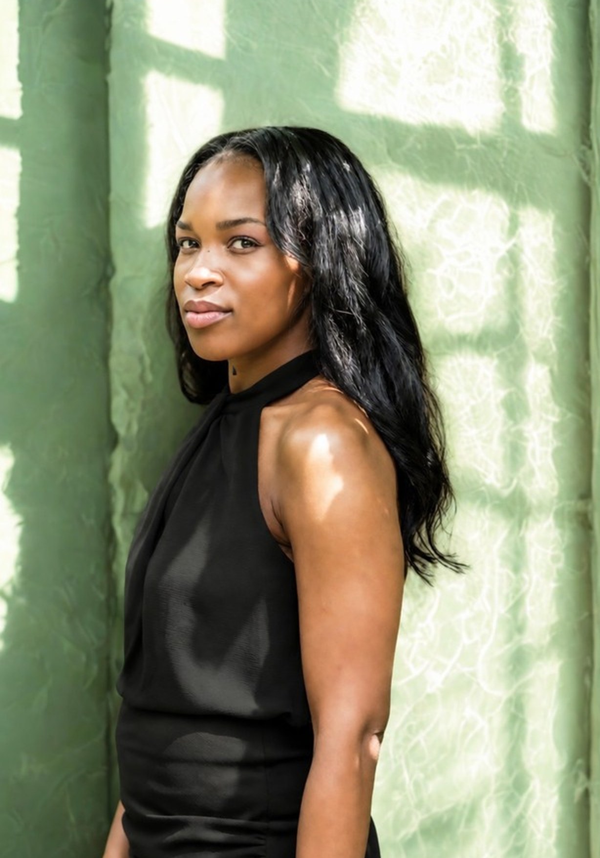 Onye, Cognitive Behavioural Hypnotherapist and founder of Your Mind Story, against a green wall